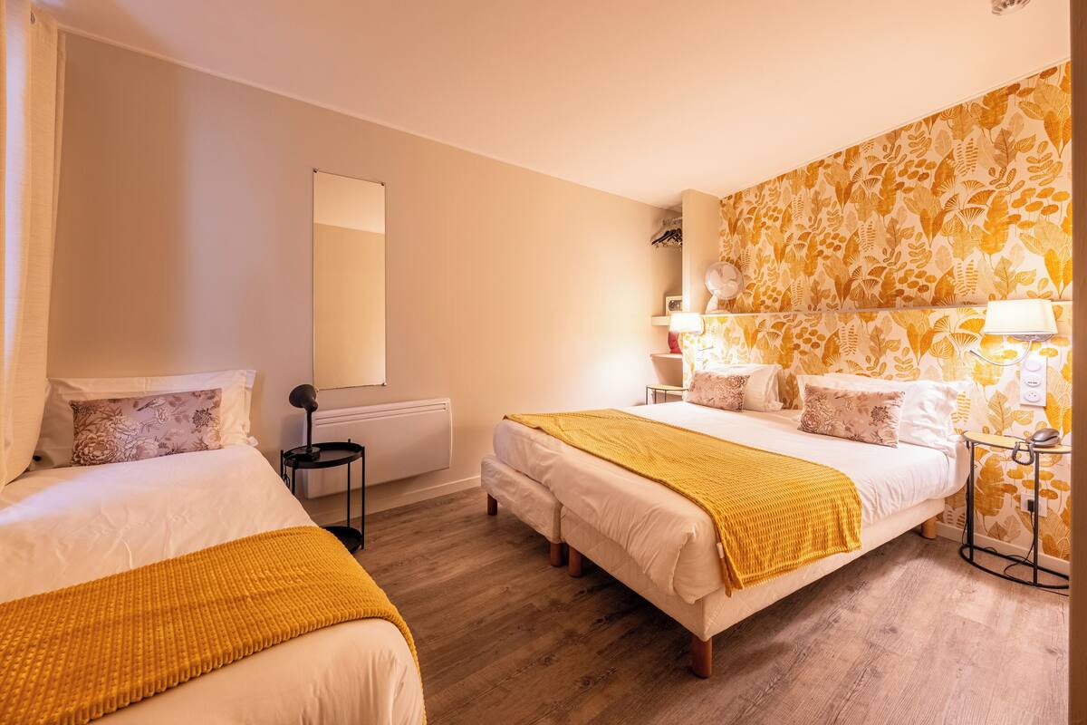 A hotel room with two beds, a large mirror, a patterned wall, and a bedside table with a lamp.