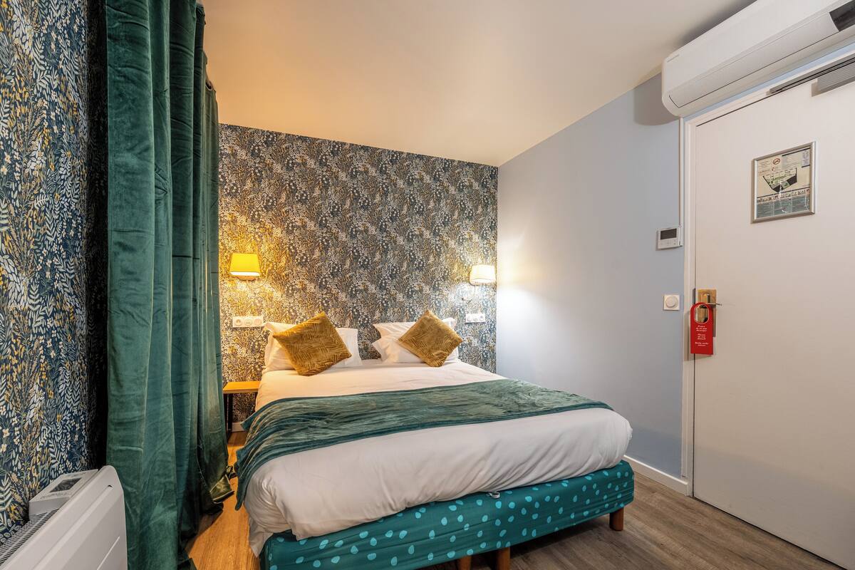 A neatly arranged bedroom with a bed, bedside lamps, a patterned wall, and a door with a sign.