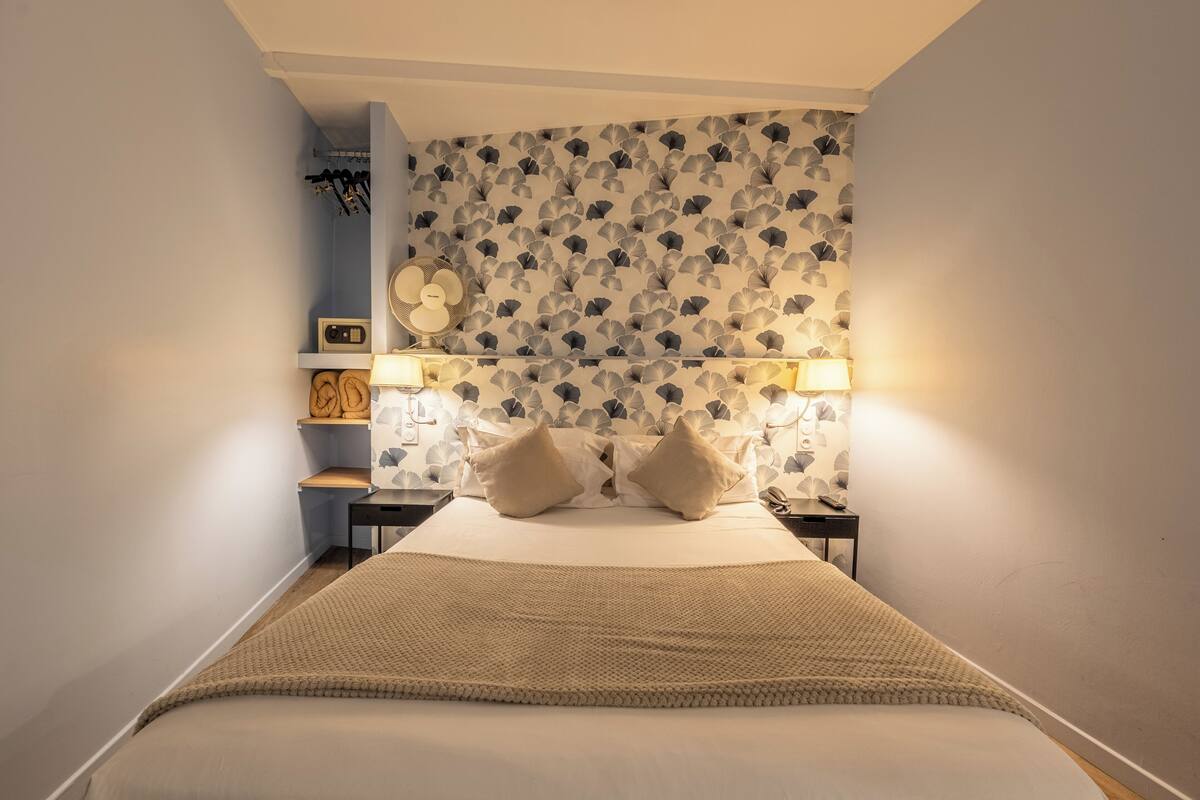 A neatly arranged bedroom with a bed, two bedside lamps, a nightstand, and a wall-mounted clock.