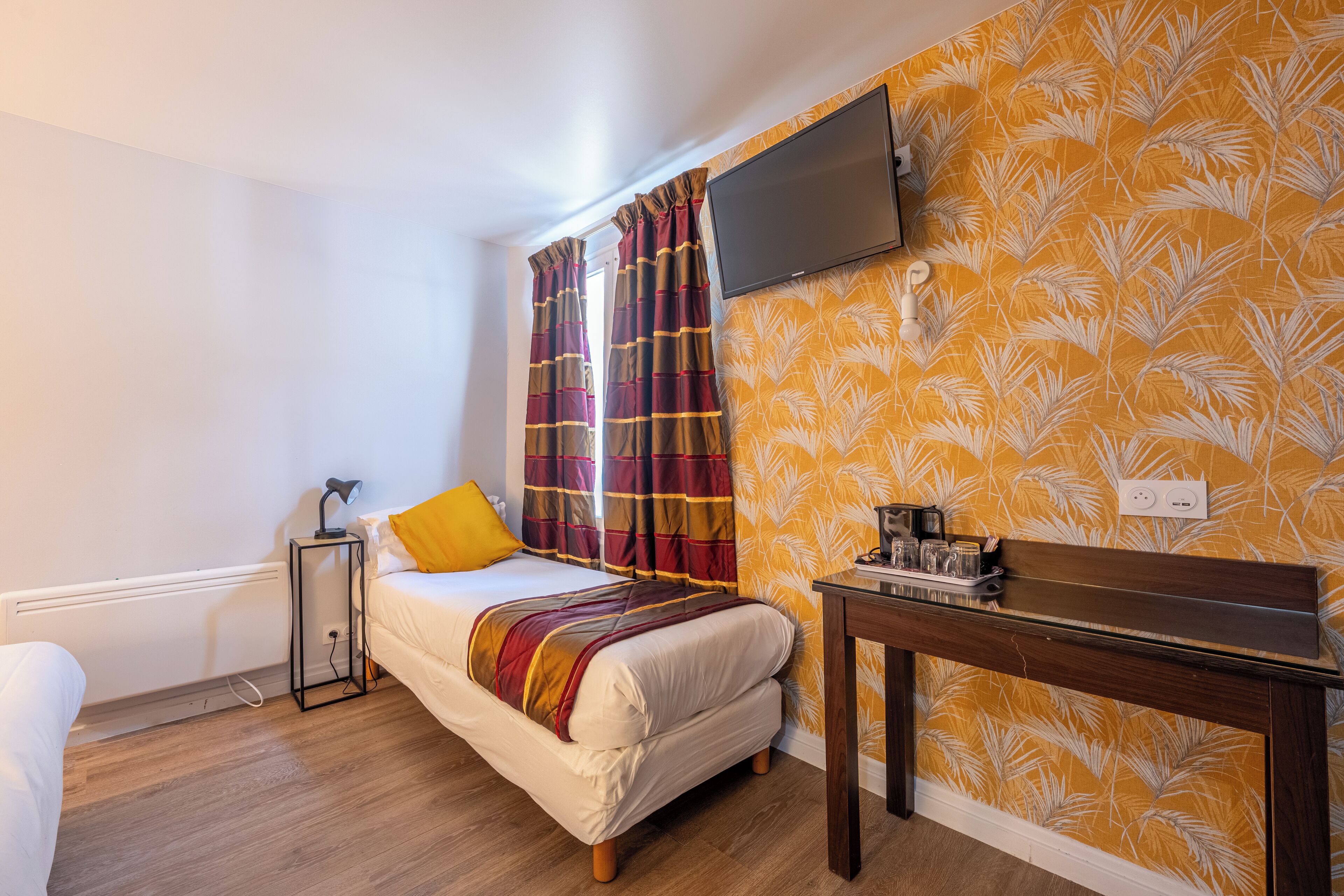 A bedroom with a bed, a bedside table, a TV mounted on the wall, and curtains.