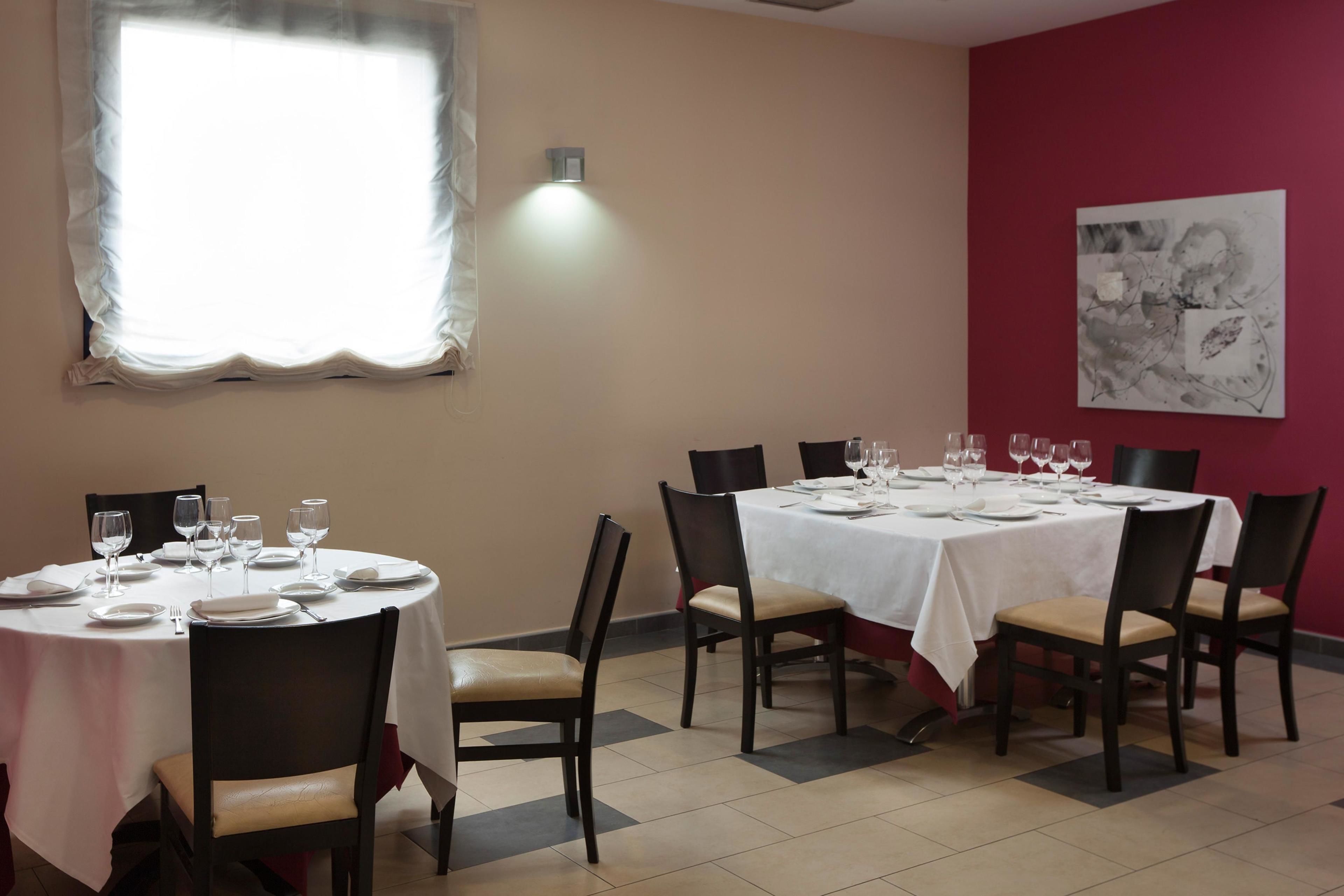 Un área de comedor con mesas redondas dispuestas para cuatro, cada una con sillas, platos, cubiertos y copas de vino.