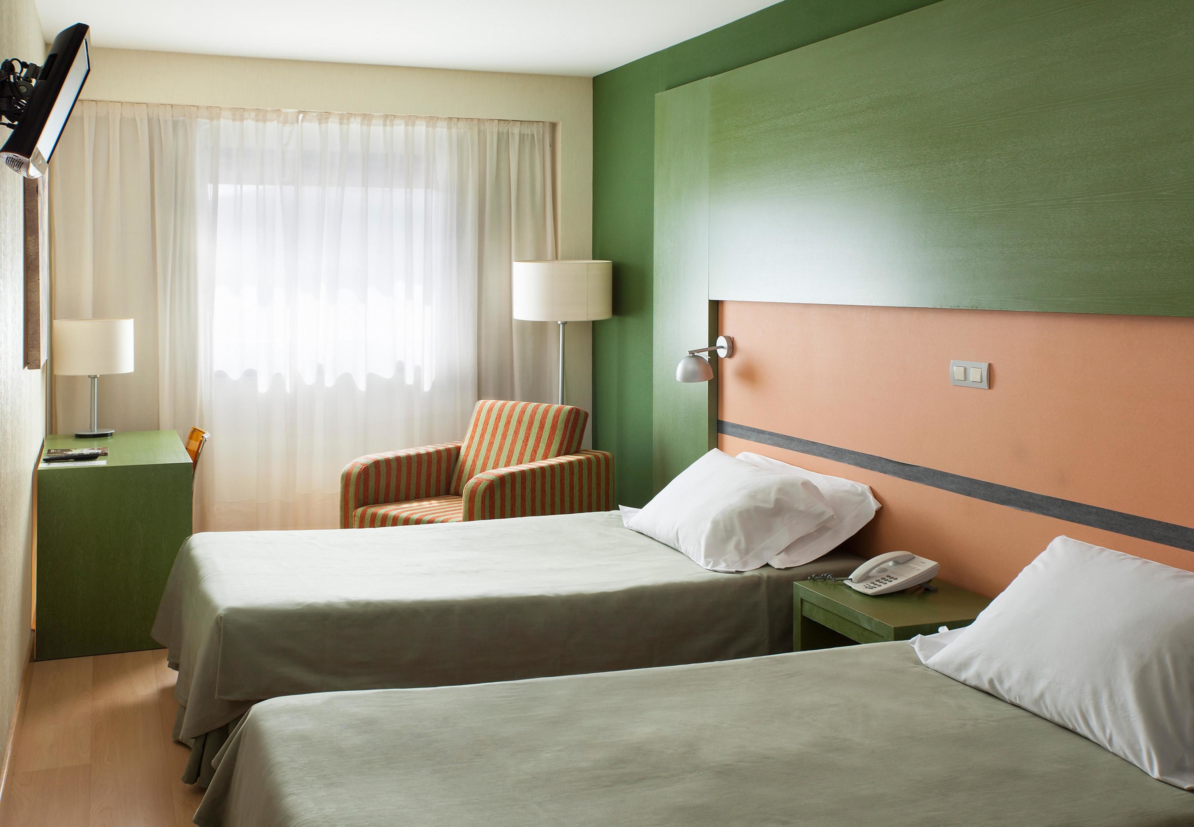 Ein Hotelzimmer mit zwei Betten, einem Sessel, einem Schreibtisch und einem Telefon.