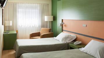 Ein Hotelzimmer mit zwei Betten, einem Sessel, einem Schreibtisch und einem Telefon.