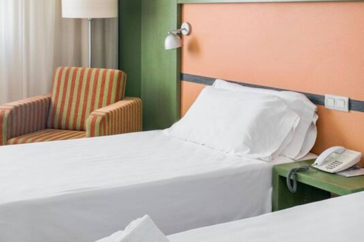 A hotel room with two beds, a striped armchair, a lamp, and a telephone on a nightstand.