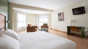 Una habitación de hotel con una cama grande, dos sillones, un escritorio y una televisión.