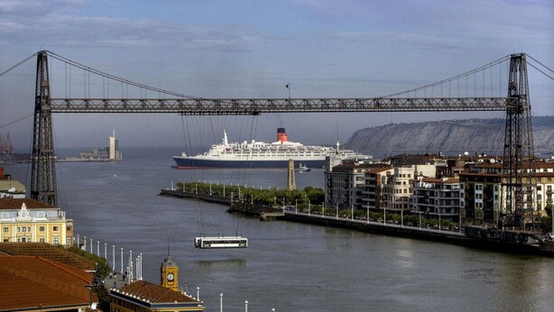 Un gran crucero amarrado en un puerto con un puente sobre él y edificios al fondo.