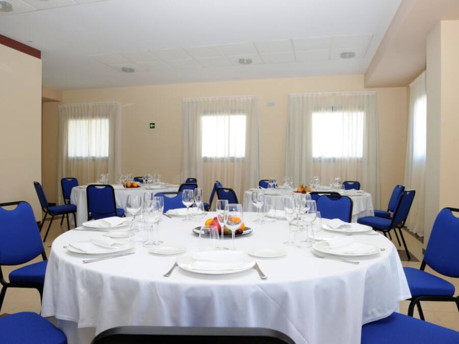 Un salón de conferencias con mesas redondas, sillas azules, manteles blancos y cristalería.