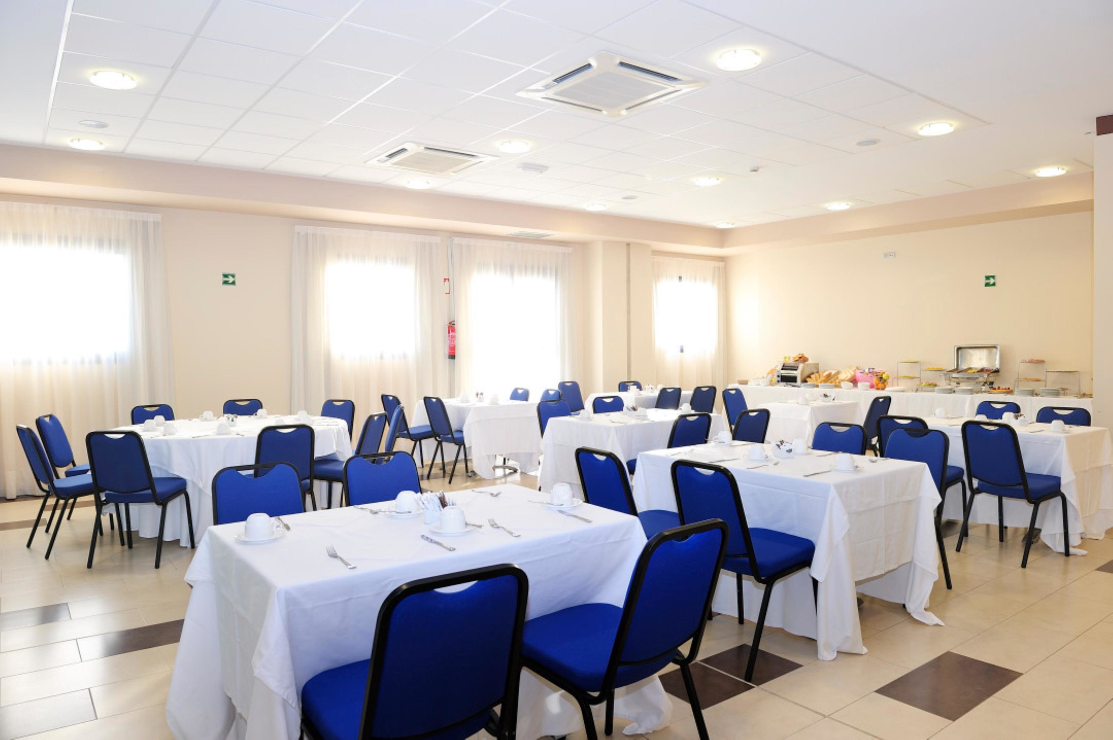A conference room with multiple tables and chairs, arranged in rows, with white tablecloths and blue chairs.