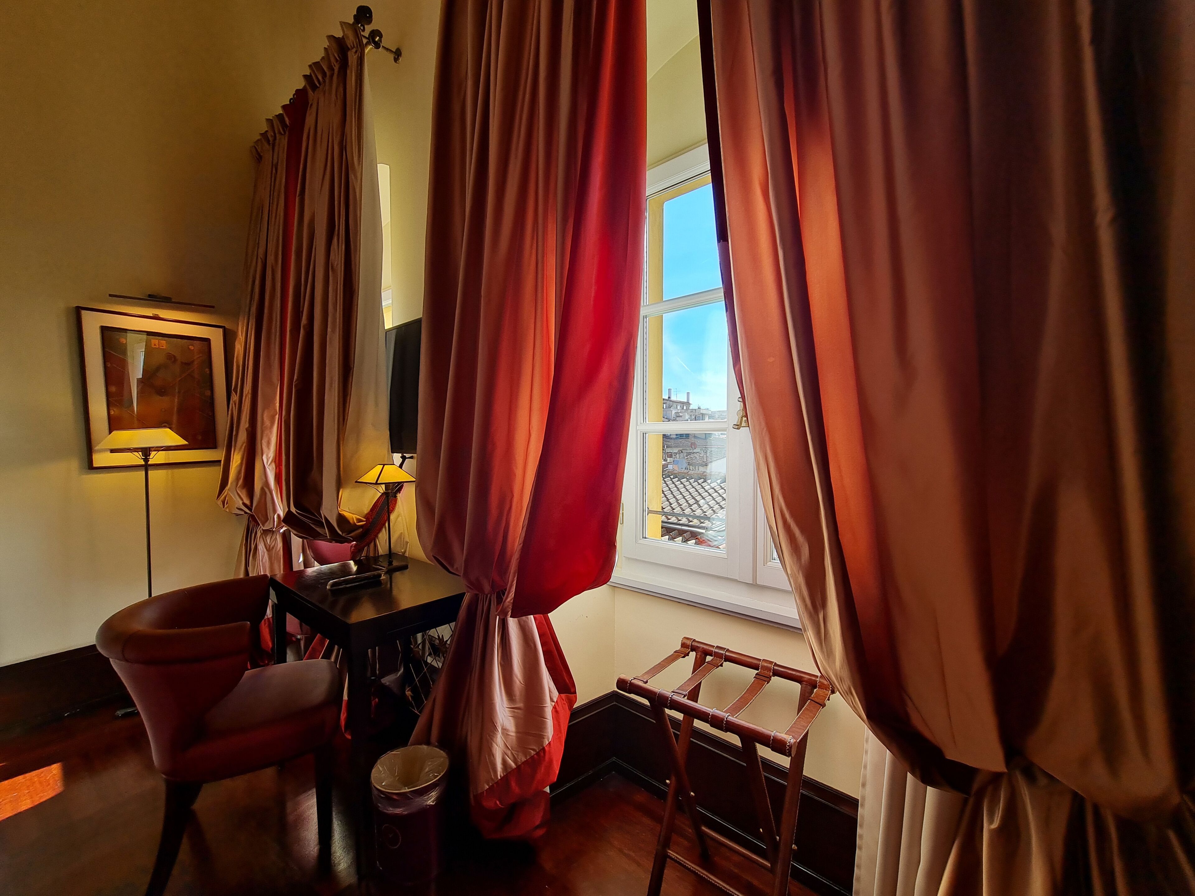 Una habitación con escritorio, silla, lámpara y ventana con cortinas.
