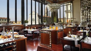 A spacious dining area with high ceilings, large windows, and a view of a historic building. Tables are set with breakfast items and a central bar area. - Hotel L'Orologio Firenze (Florence)