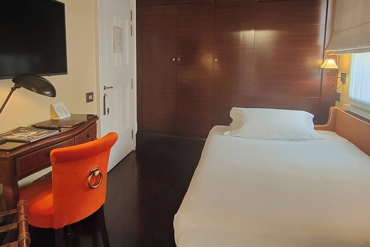 A hotel room with a bed, a desk with a chair, a television, and a door.