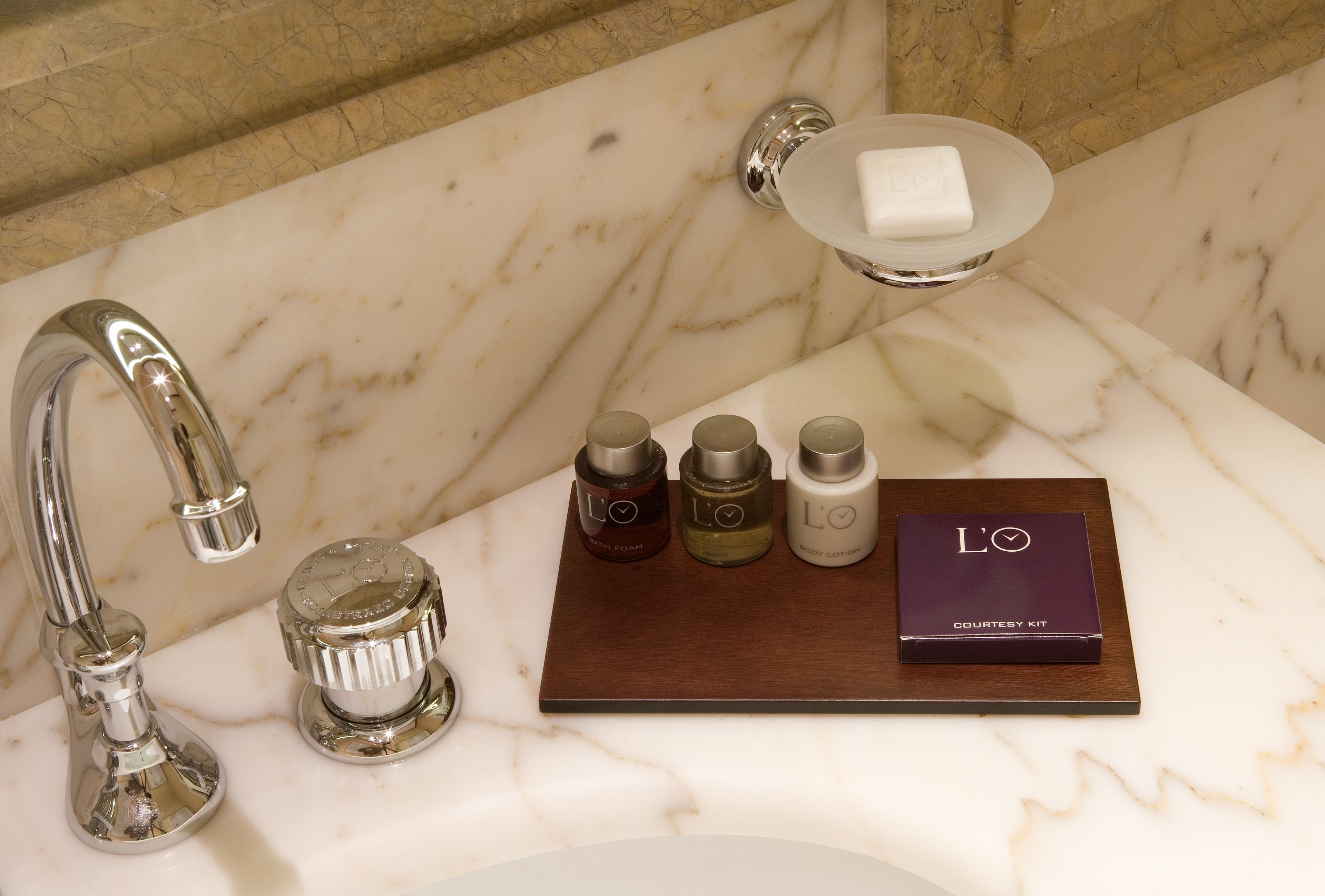 A bathroom with a marble sink, a faucet, a soap dish, and a courtesy kit.