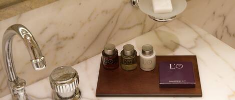 A bathroom with a marble sink, a faucet, a soap dish, and a courtesy kit.