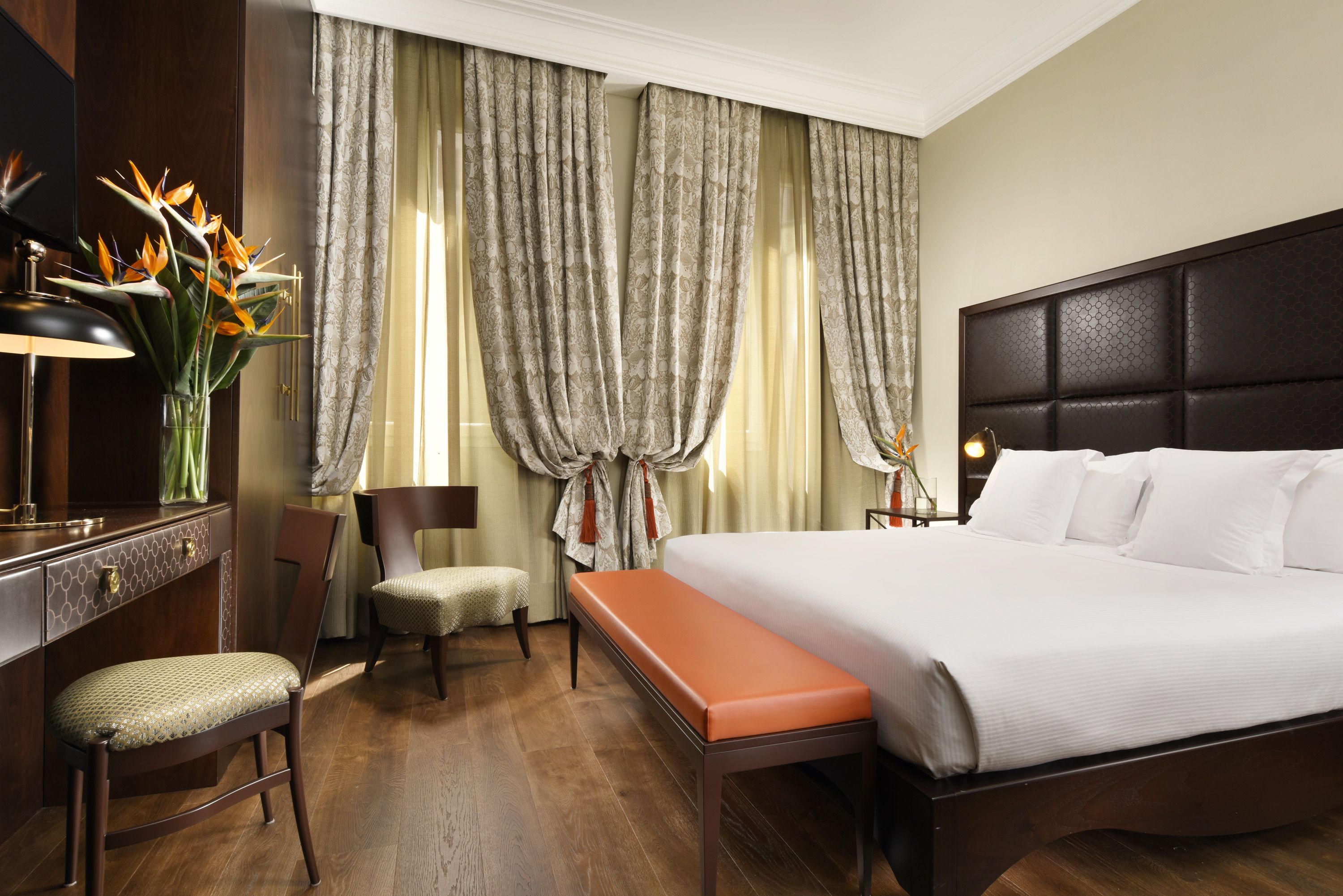 Una habitación de hotel con una cama grande, un escritorio con lámpara, una silla y un banco.