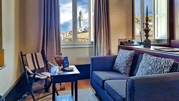 Una habitación con vistas a una torre, un sofá, una silla, una mesa con un vaso y un libro, y una ventana con cortinas.