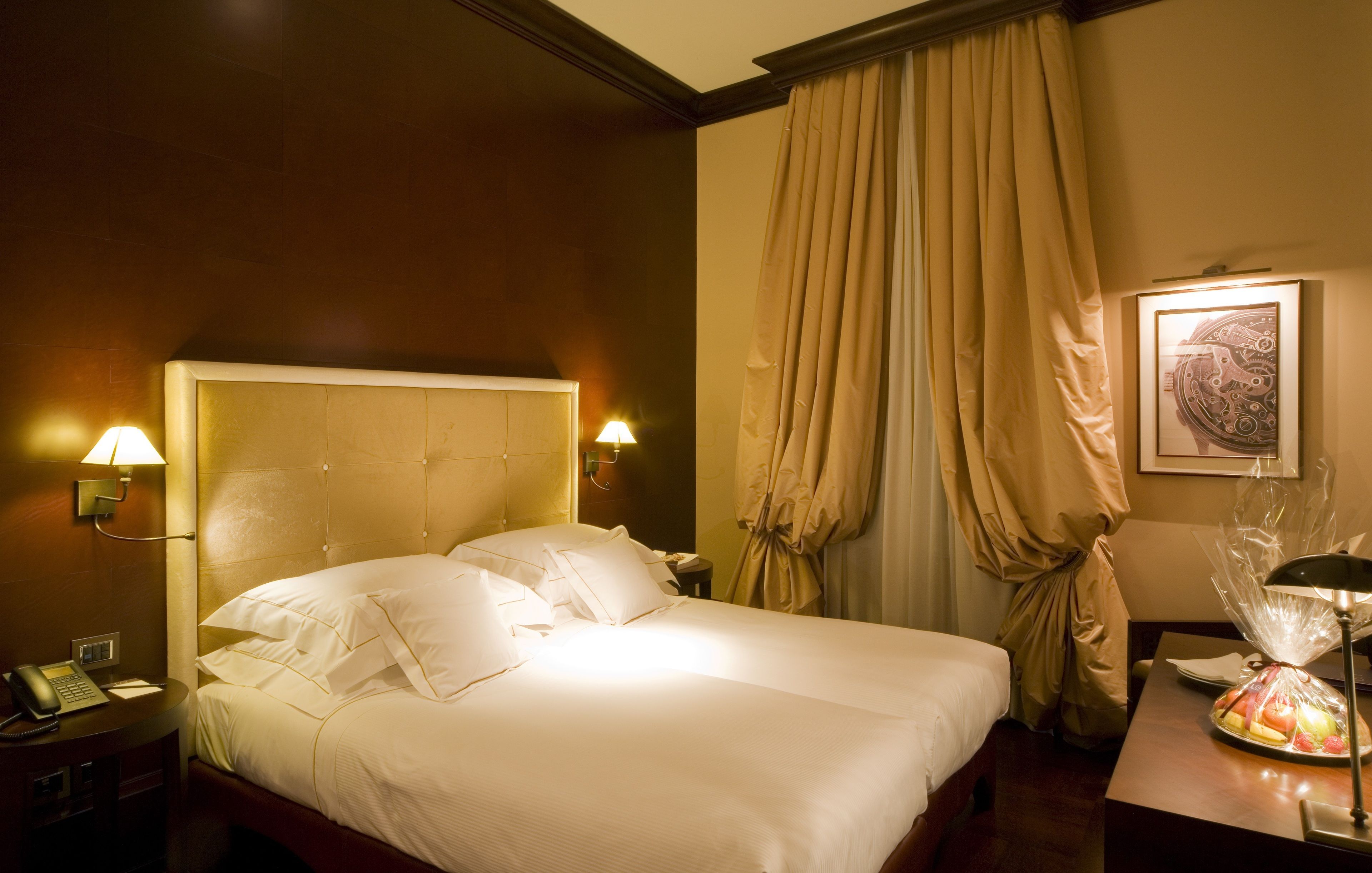 A hotel room with a large bed, bedside lamps, a telephone, and a fruit basket on the nightstand.