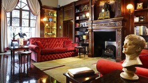 A library with a red sofa, bookshelves, a fireplace, and a bust on a table. - Hotel L'Orologio Firenze (Florence)