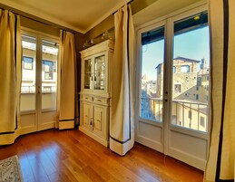Una stanza con pavimento in legno, un armadietto bianco con ante in vetro e vista sugli edifici attraverso ampie finestre.