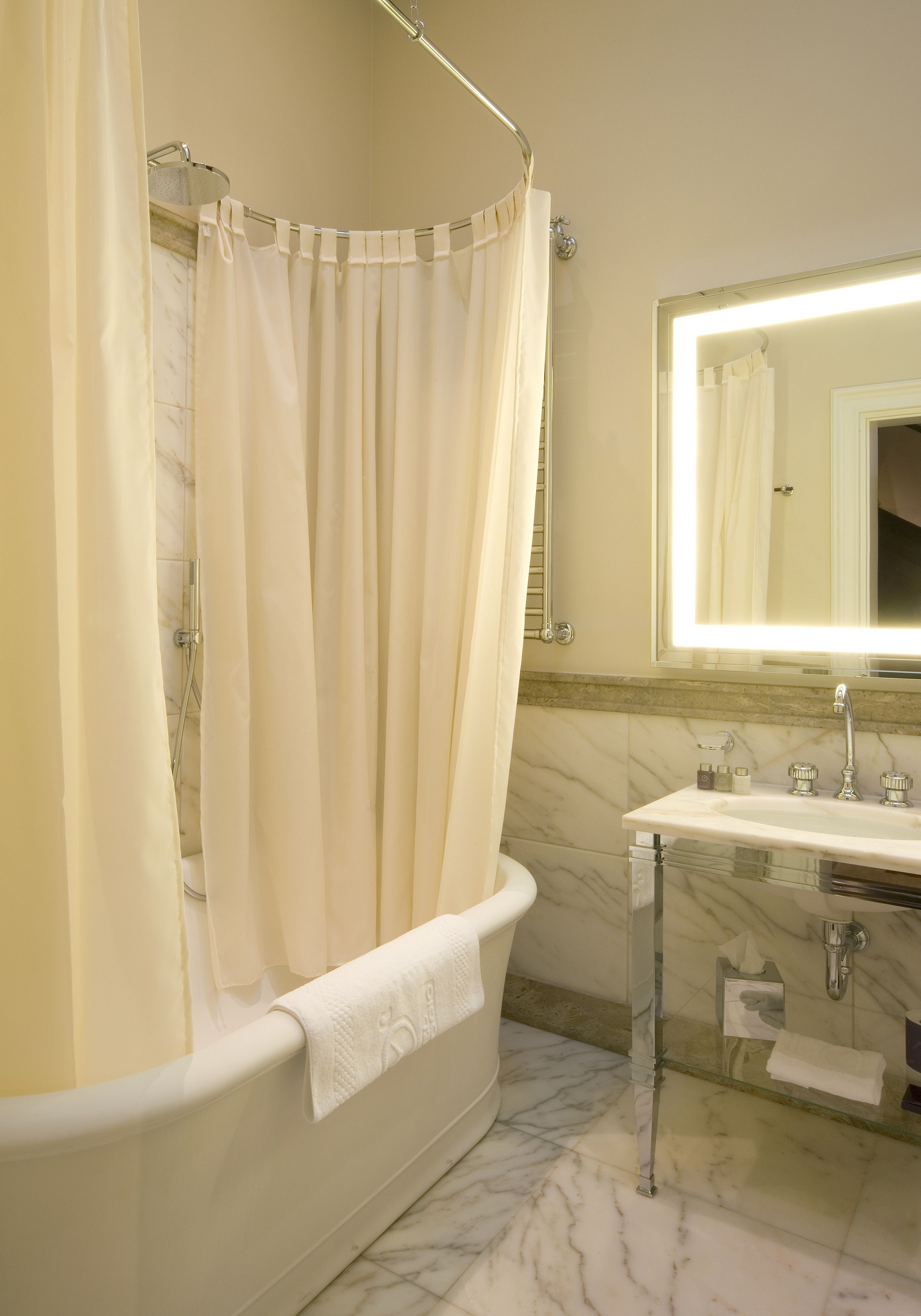 A bathroom with a bathtub, a glass-enclosed sink, and a mirror with a light.