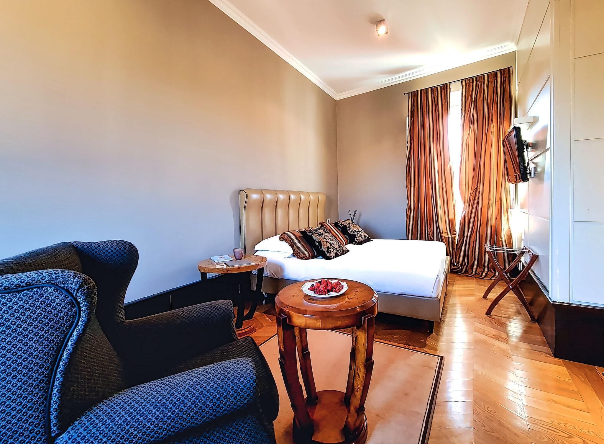 Ein Hotelzimmer mit Bett, kleinem runden Tisch mit Früchten, einer Couch und einem Fernseher an der Wand.