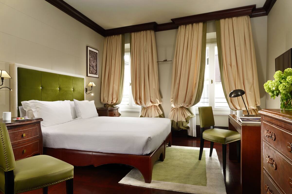 A hotel room with a large bed, a desk, a chair, a dresser, and curtains.