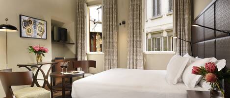 A hotel room with a large bed, a desk with a chair, a TV, and a window with curtains.
