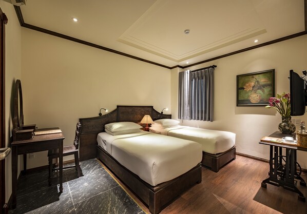 Habitación de hotel con dos camas, un escritorio, una silla, un televisor y un cuadro en la pared.