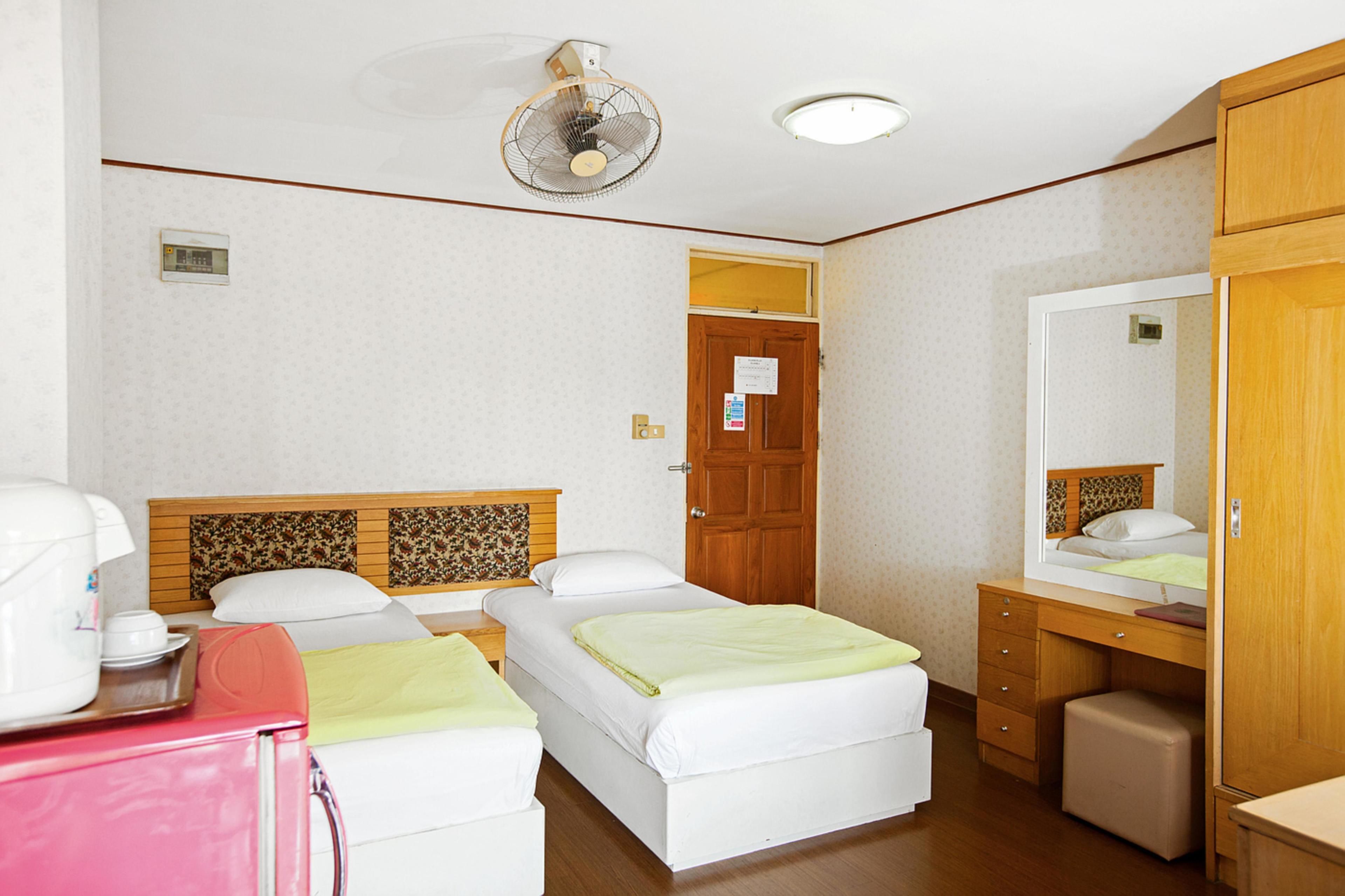 A hotel room with two beds, a wooden headboard, a desk, a chair, a mirror, and a ceiling fan.