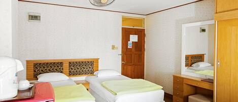 A hotel room with two beds, a wooden headboard, a desk, a chair, a mirror, and a ceiling fan.