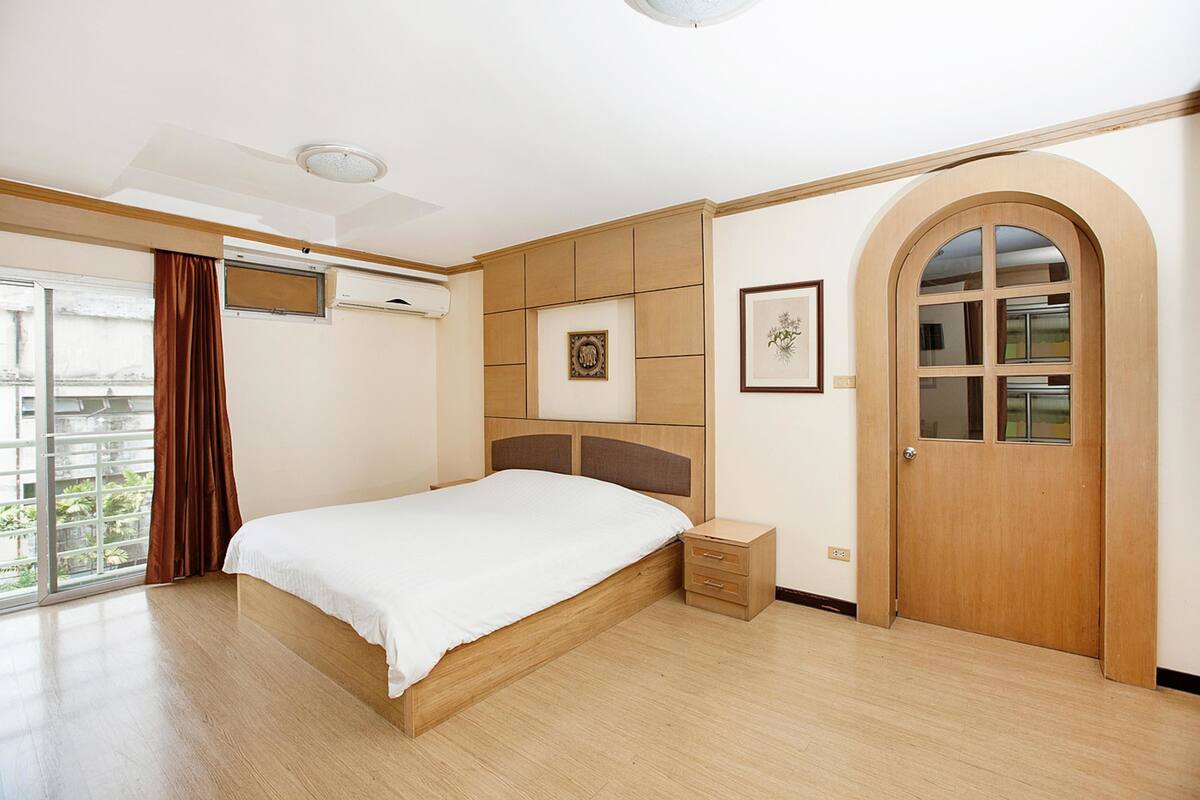 Un dormitorio con una cama de madera, una mesita de noche pequeña, un armario y un ventanal grande de arco.