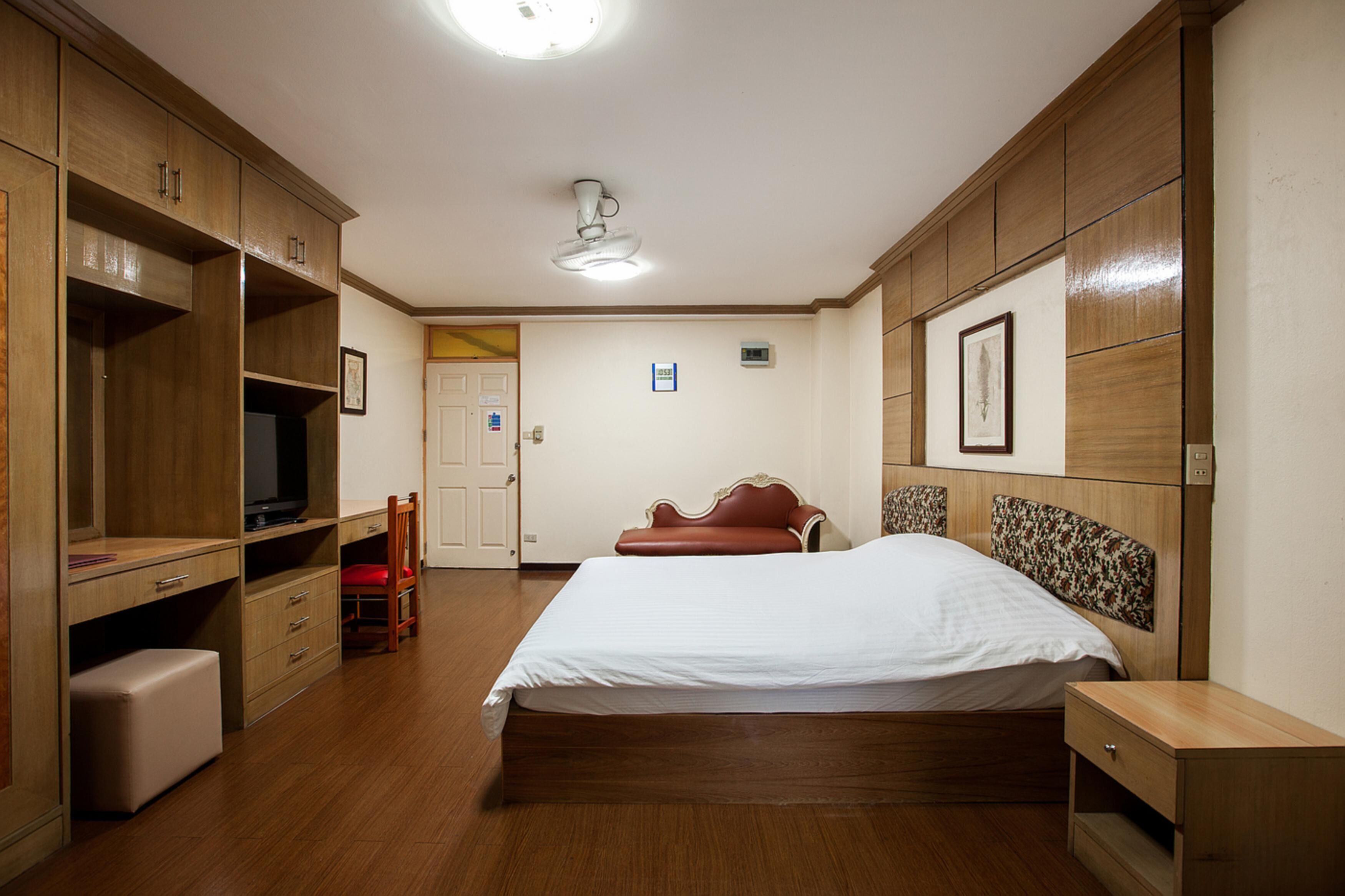 A bedroom with a bed, wooden wardrobe, a desk, and a television.