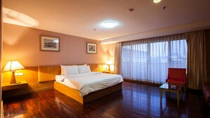 Een hotelkamer met een houten bed, twee bedlampen, een rode stoel en een groot raam met dunne gordijnen.