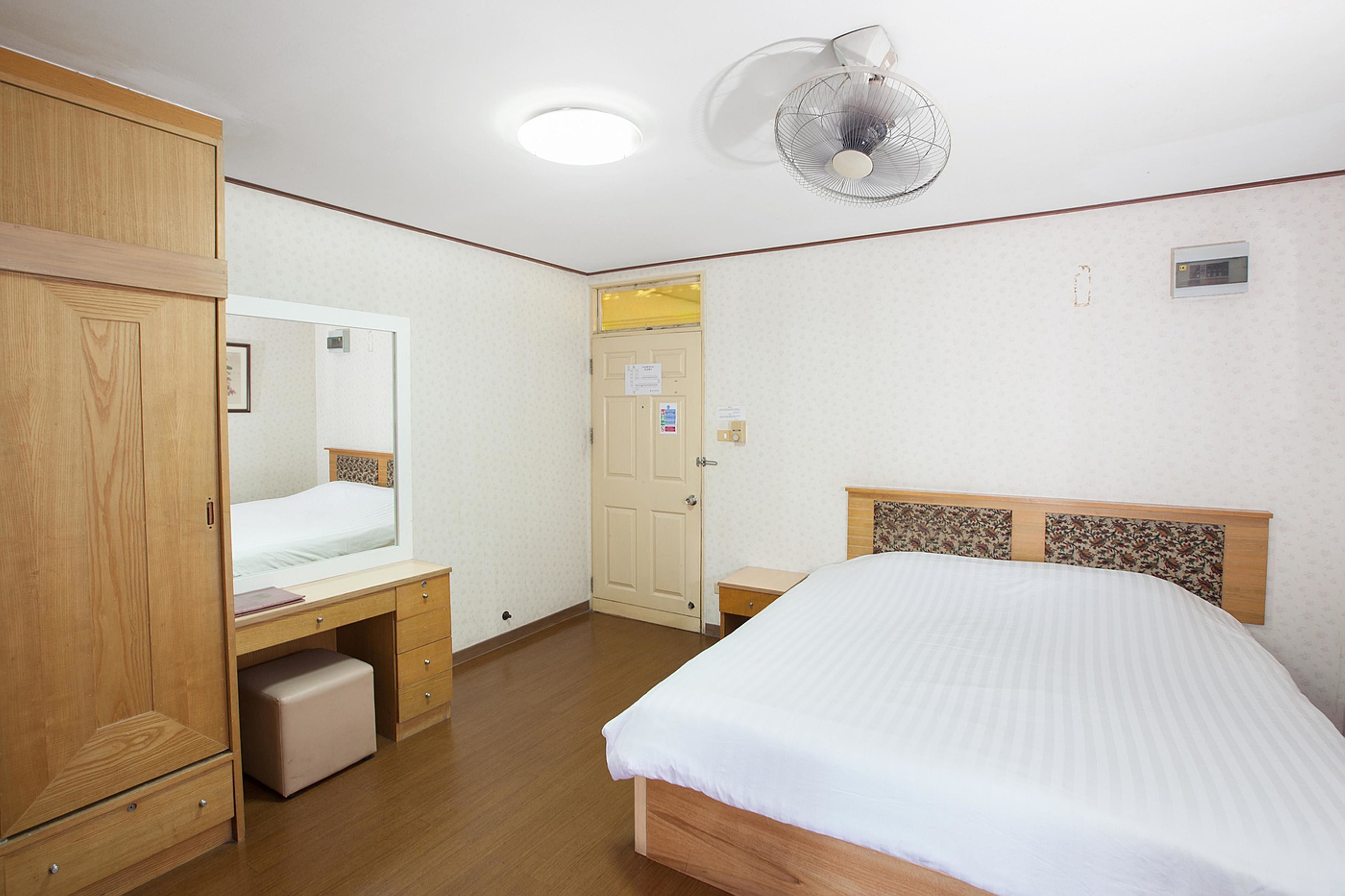 A bedroom with a bed, wooden wardrobe, bedside table, and a ceiling fan.