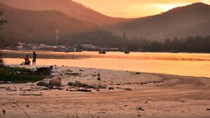 Escena ribereña con un puente, barcos y un paisaje montañoso al atardecer.