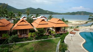 Un resort con varias construcciones tipo bungalow, una piscina y vista al mar.