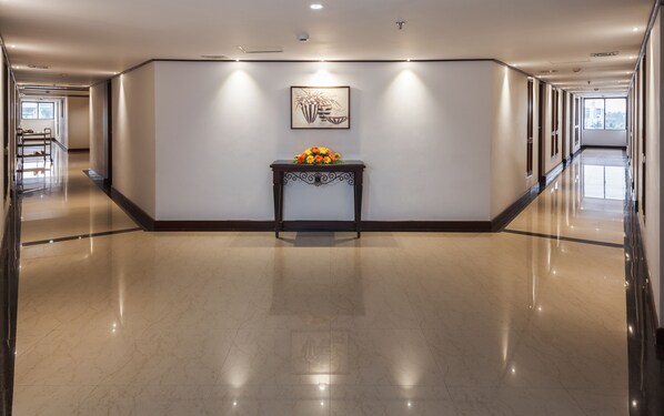 A spacious hallway with a polished marble floor, a dark wooden console table with a vase of flowers, and a framed artwork on the wall. - Keys Select by Lemon Tree Hotels, Malabar Gate, Kozhikode (Kozhikode)