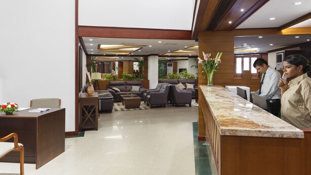A hotel lobby with a reception desk, seating area, and decorative plants.