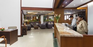 A hotel lobby with a reception desk, seating area, and decorative plants.
