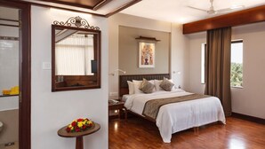 A hotel room with a bed, a bedside table with a lamp, a mirror, a painting, and a window with curtains.