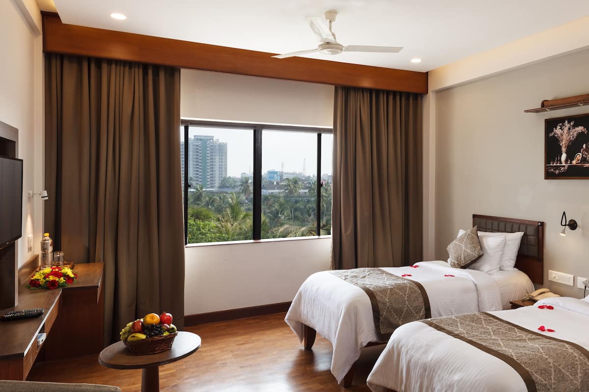 A hotel room with two beds, a TV, a small table with fruit, and a view of the city.