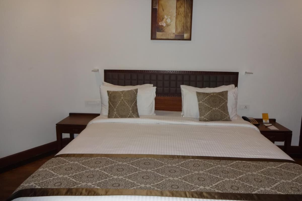 A hotel room with a large bed, a headboard, two bedside tables, and a painting above the bed.
