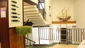A hotel lobby with a staircase, a ship model, a signboard with room directions, and a small plant.