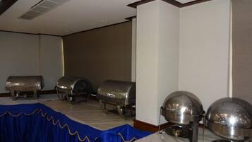 A room with a long table covered by a blue tablecloth, lined with silver buffet trolleys and a large silver urn.