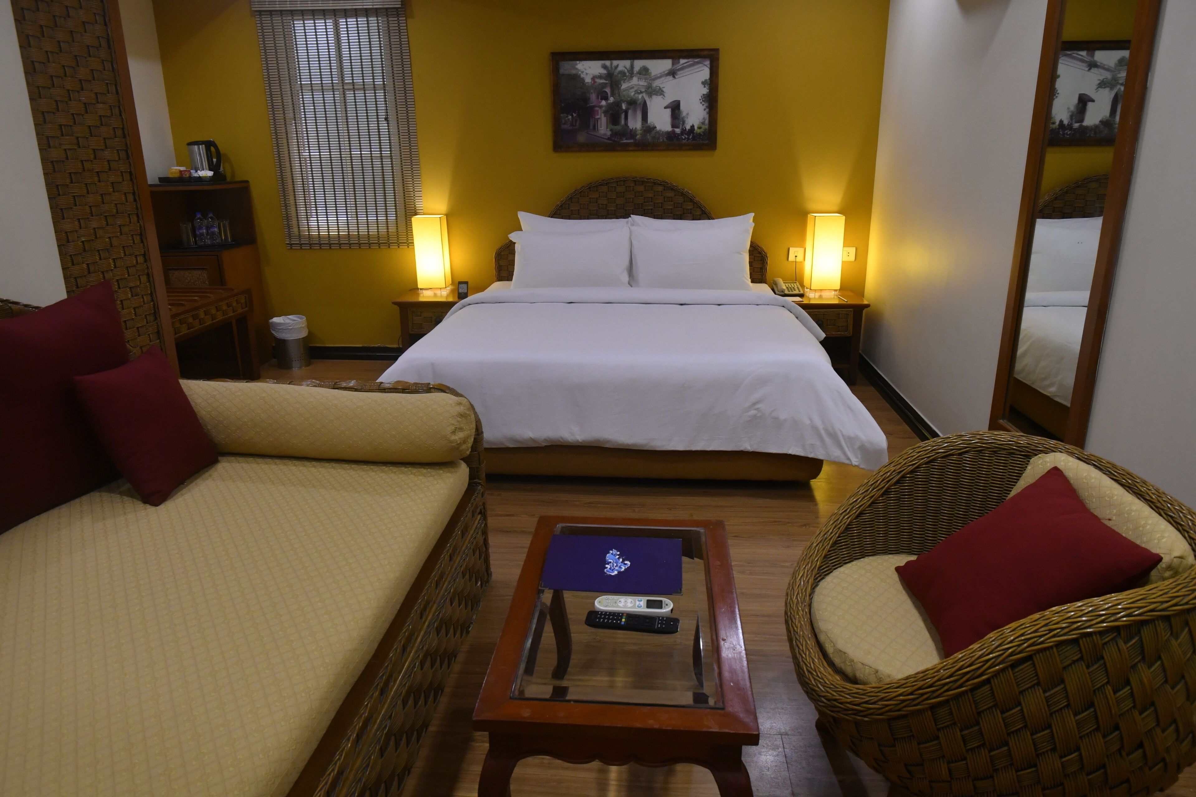 Habitación de hotel con cama, dos sofás, una mesita con un control remoto y una silla de mimbre.