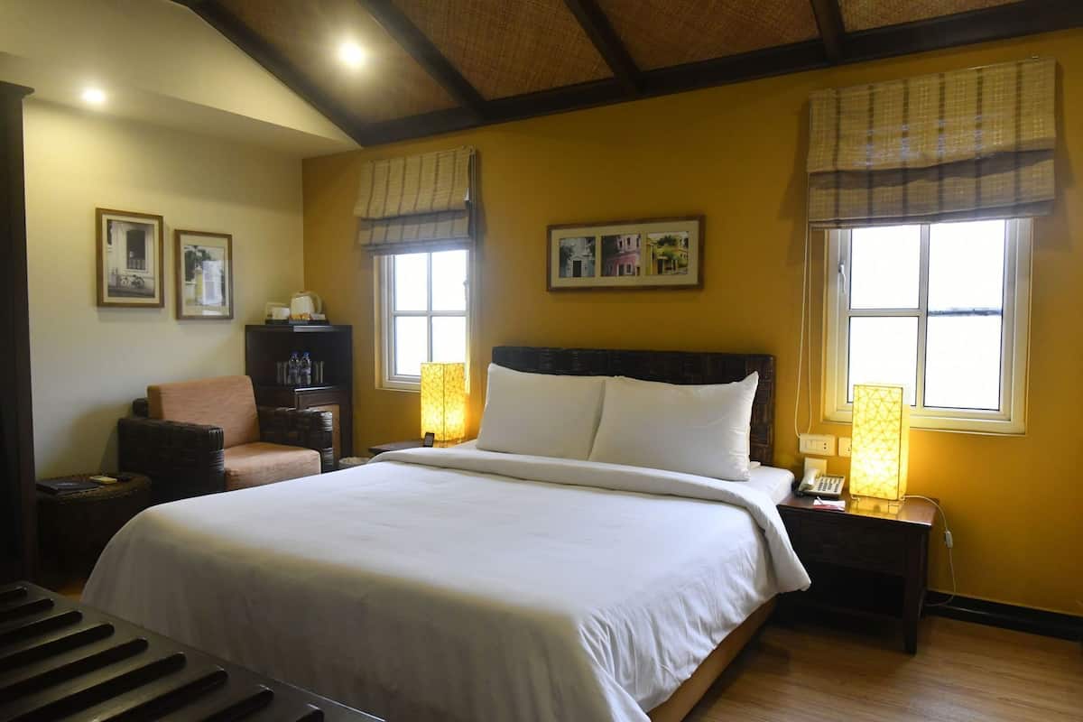 Una habitación de hotel con una cama grande, dos mesitas de noche, una silla y cuadros en la pared.