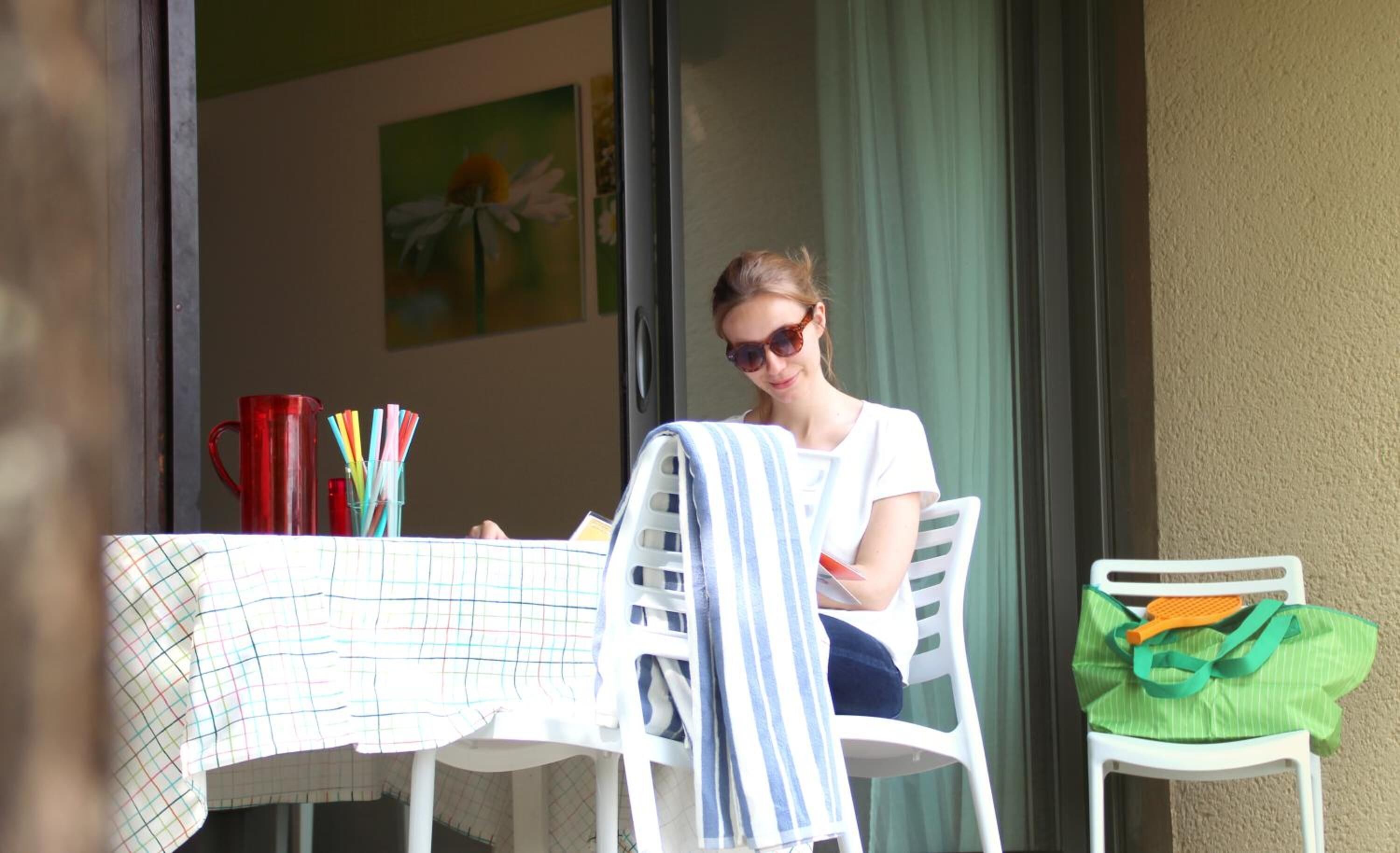 A person seated at a table with a striped towel draped over the chair, a red mug, and a green bag on the table.