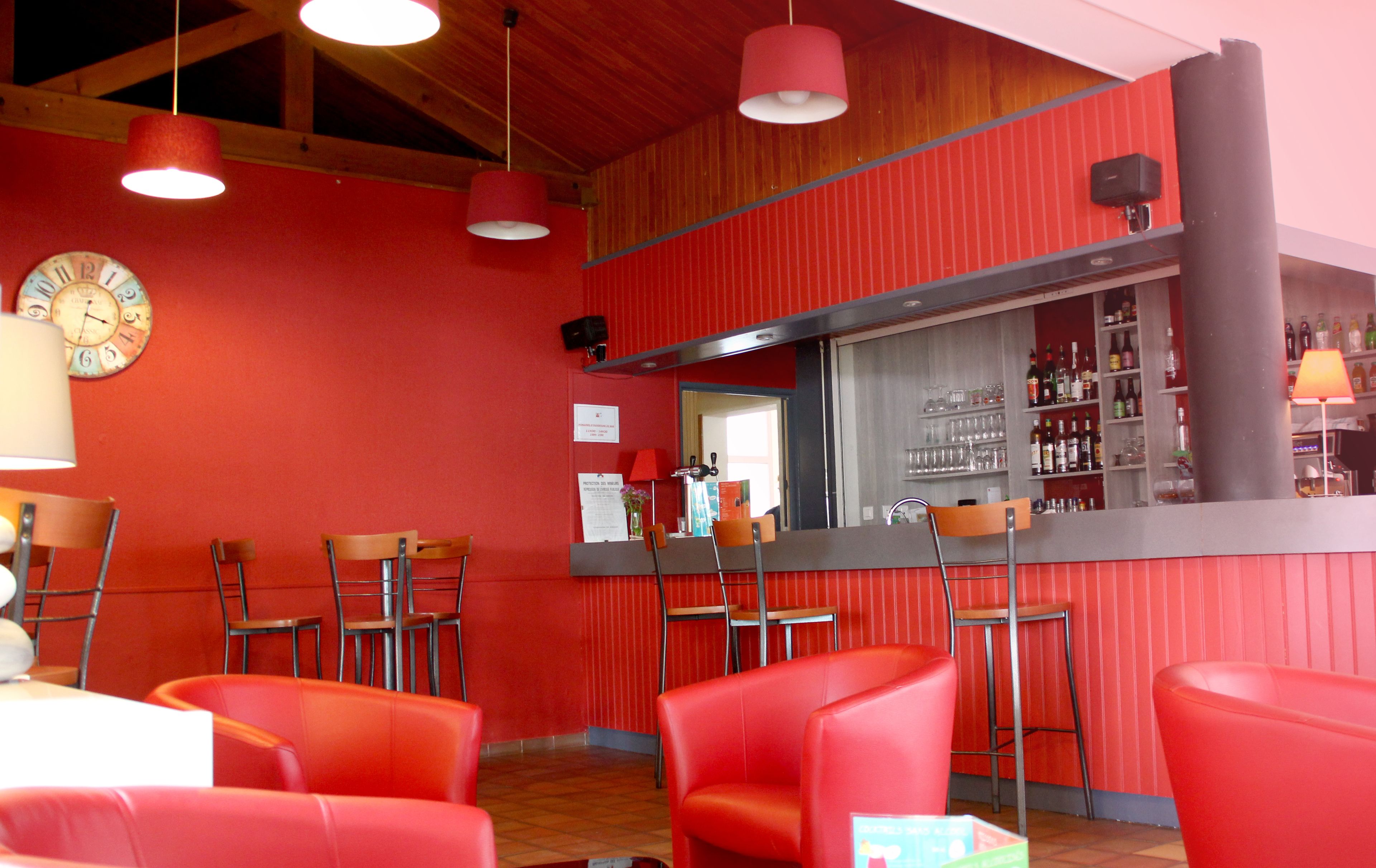 A restaurant interior with red walls, multiple red chairs, a bar area with shelves of bottles, and hanging pendant lights.