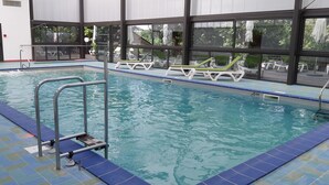 Une piscine intérieure à l’eau d’un bleu cristallin, avec une terrasse carrelée et des chaises longues disposées tout autour.
