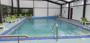 An indoor swimming pool with clear blue water, surrounded by white walls and large windows.