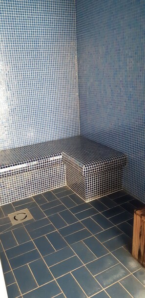 A tiled bathroom with a bench and a wooden stool.